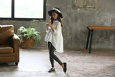 Girl in oversized white asymmetrical shirt, black skinny jeans, floppy hat, and loafers