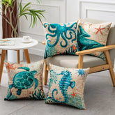 Set of four beige throw pillows with teal sea life designs, including octopus, whale, turtle, and seahorse, in a modern living room setting.