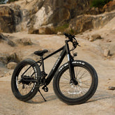 Matte black fat tire mountain bike with wide 26-inch wheels on rocky outdoor terrain