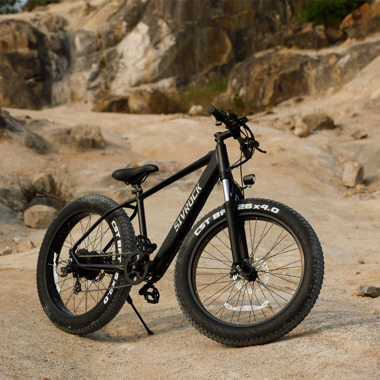 Matte black fat tire mountain bike with wide 26-inch wheels on rocky outdoor terrain