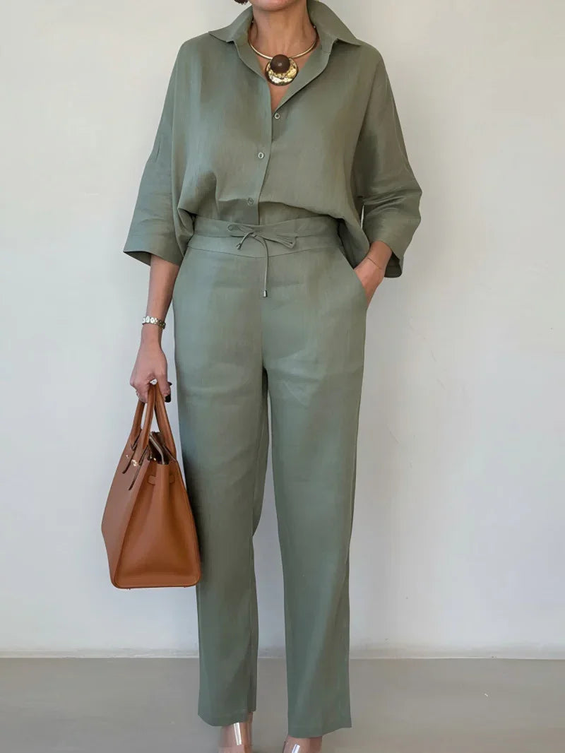 Woman wearing loose-fit sage green linen shirt and pants set, carrying a tan handbag