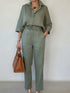 Woman wearing loose-fit sage green linen shirt and pants set, carrying a tan handbag