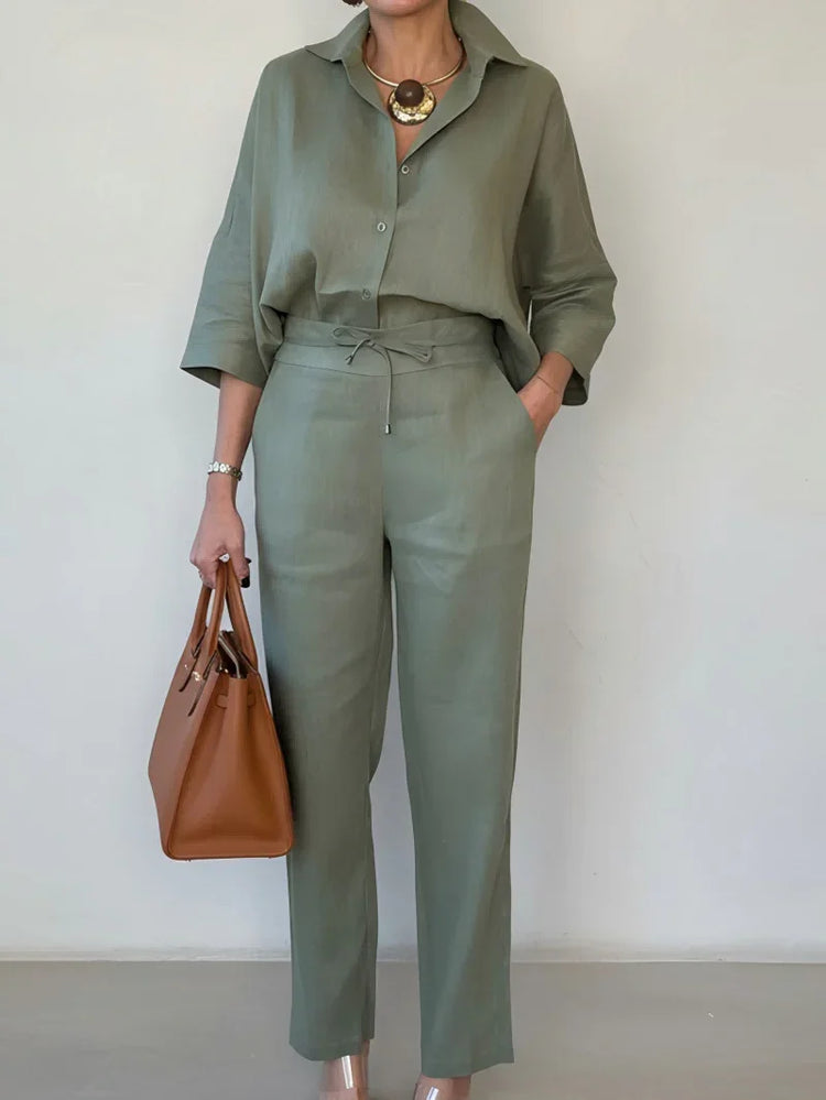 Woman wearing loose-fit sage green linen shirt and pants set, carrying a tan handbag