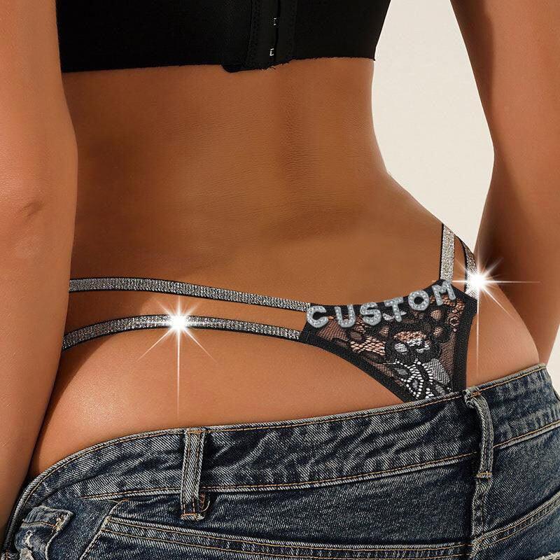 Black lace thong with rhinestone straps and custom text, paired with denim jeans, fitted style.