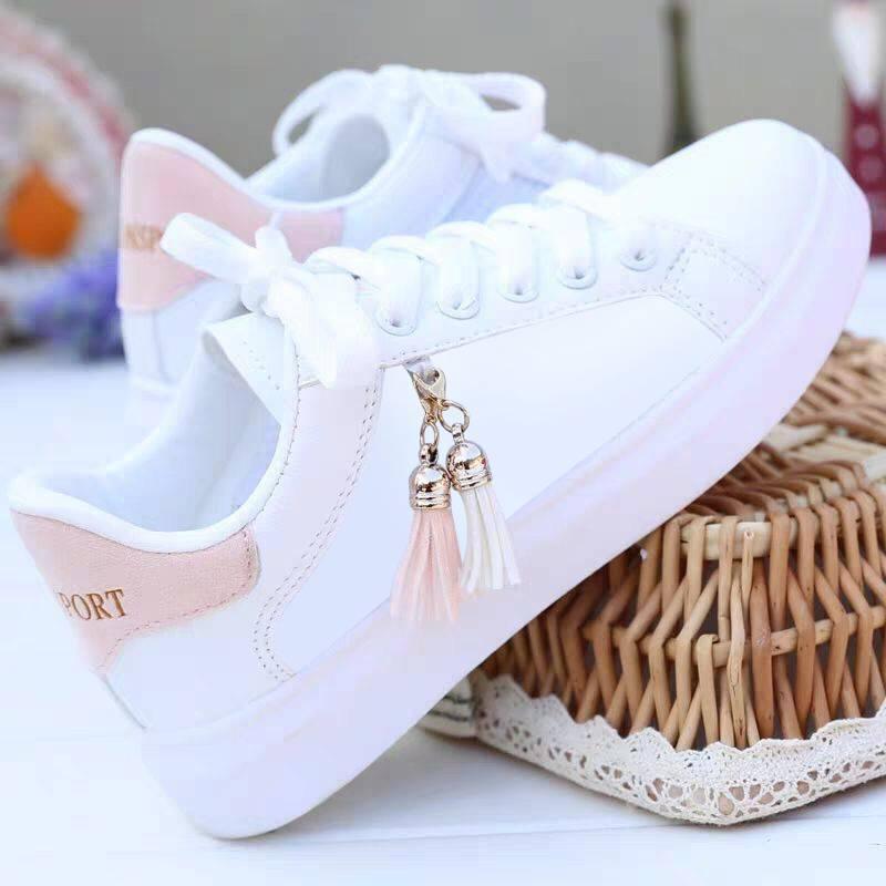 White low-top sneakers with pink accents, leather material, tassel lace charm, casual fit.
