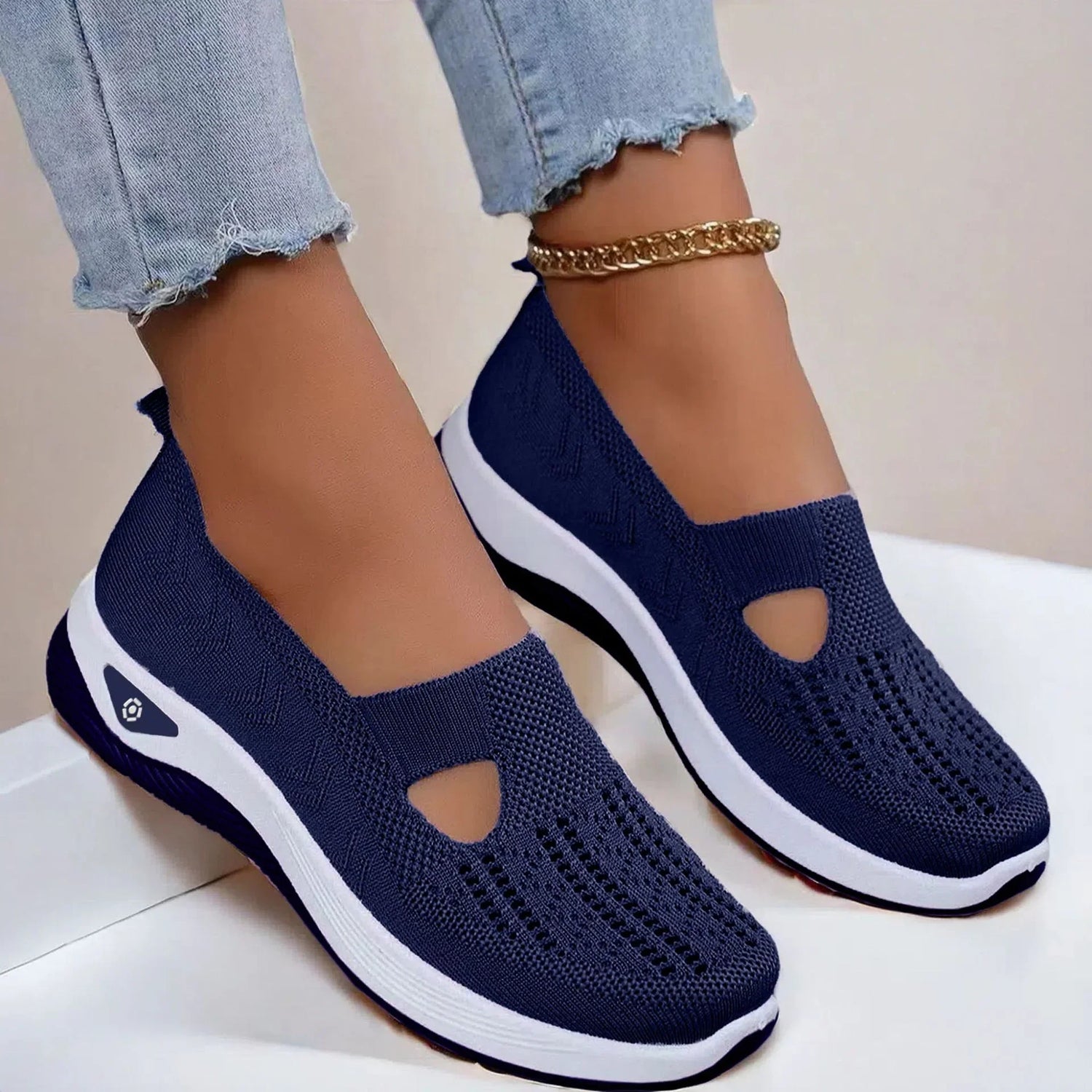 Navy blue knit slip-on sneakers with white soles and breathable mesh design, shown with frayed light denim jeans.
