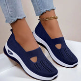 Navy blue knit slip-on sneakers with white soles and breathable mesh design, shown with frayed light denim jeans.
