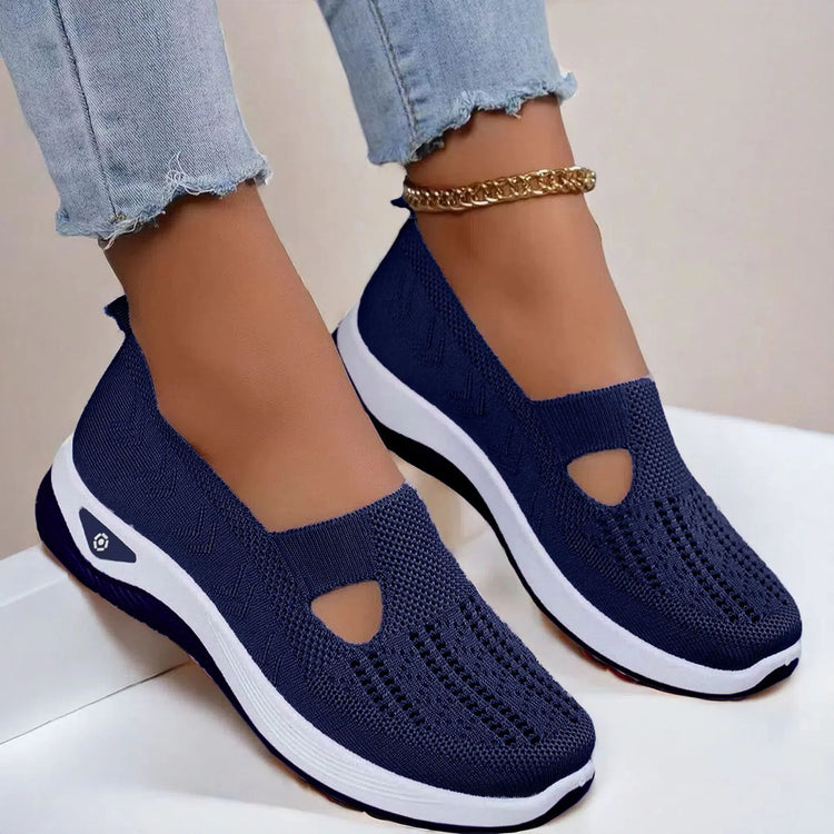 Navy blue knit slip-on sneakers with white soles and breathable mesh design, shown with frayed light denim jeans.