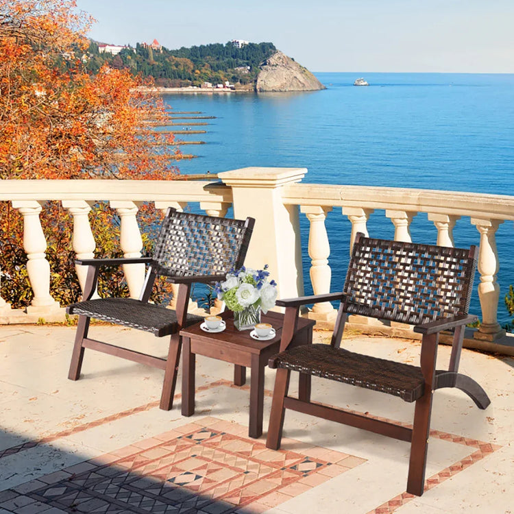 Dark brown woven rattan patio chairs and table set on a terrace overlooking the sea