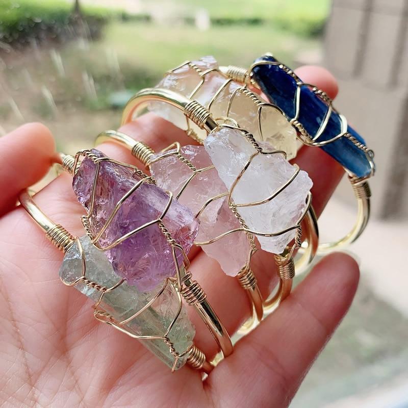Hand holding gold wire-wrapped gemstone bracelets in assorted colors, chunky and modern style.