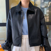 Woman wearing a black faux leather zip-up jacket with relaxed fit, blue ribbed top, and white pants.