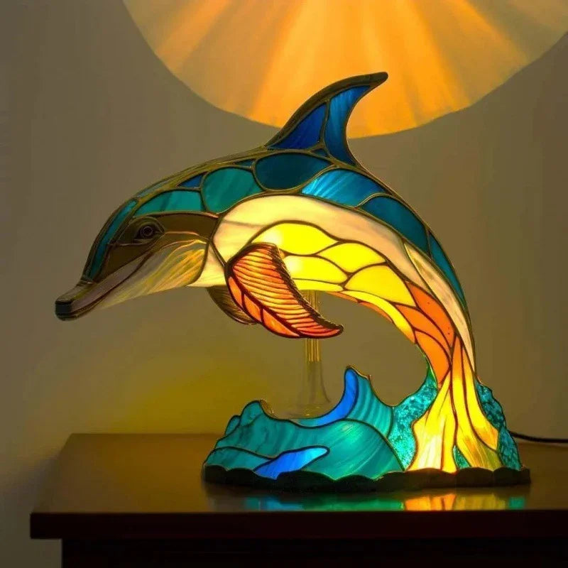 Colorful stained glass dolphin table lamp with blue, yellow, and orange tones, glowing on a nightstand.