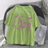 Light green oversized graphic t-shirt with purple streetwear prints, paired with ripped denim shorts.