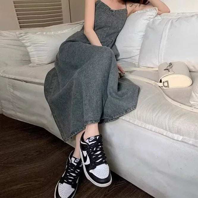 Woman in a grey denim maxi dress and black-and-white sneakers sitting on a white couch