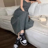 Woman in a grey denim maxi dress and black-and-white sneakers sitting on a white couch