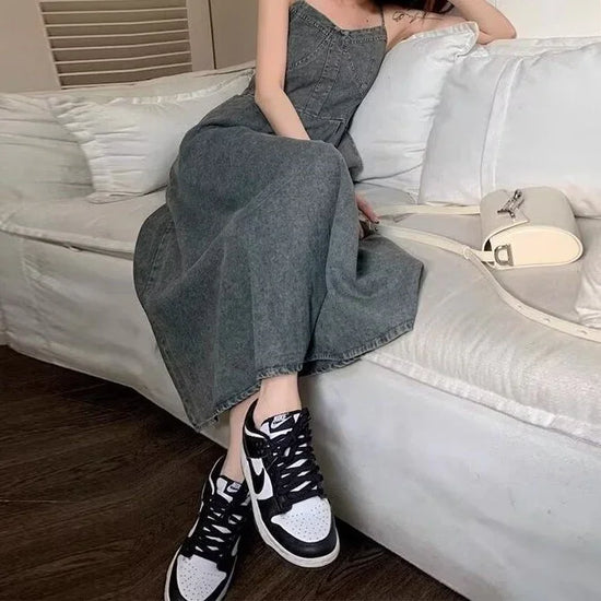 Woman in a grey denim maxi dress and black-and-white sneakers sitting on a white couch