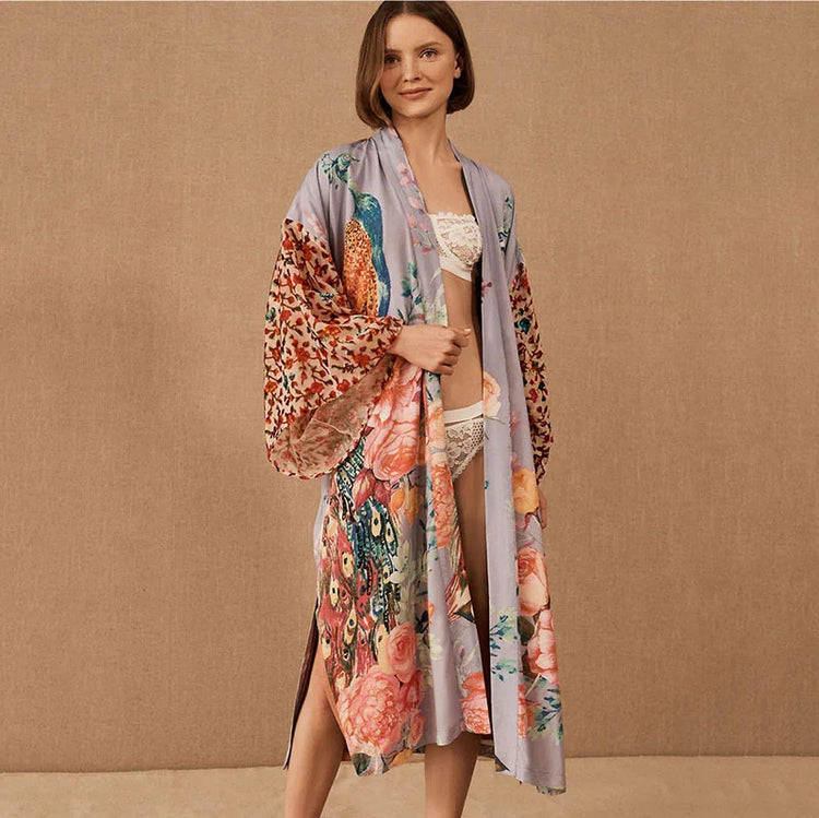 Woman wearing a long, floral kimono robe with colorful peacock and flower print, relaxed fit.