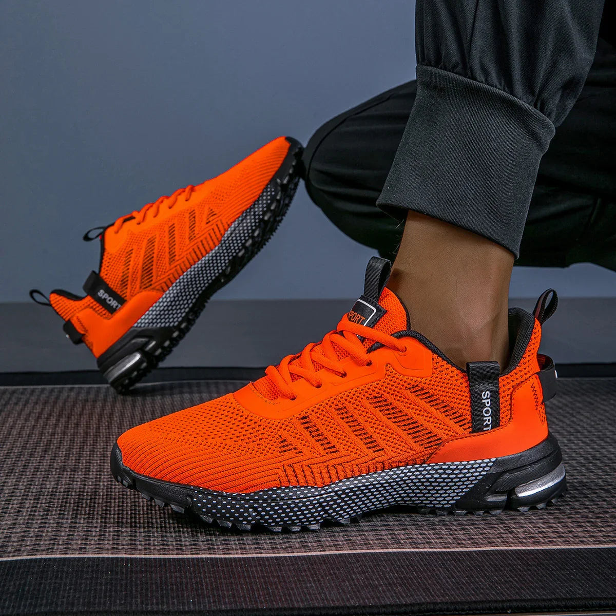 Bright orange knit athletic sneakers with black soles and mesh pattern, worn with jogger pants