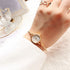 Gold-tone minimalist wristwatch with white dial on wrist, worn with white long sleeve top