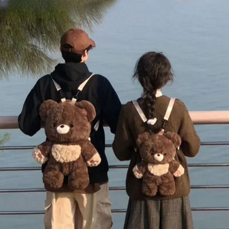 Couple wearing plush bear backpacks, casual streetwear, brown and beige layered outfits, outdoor setting.