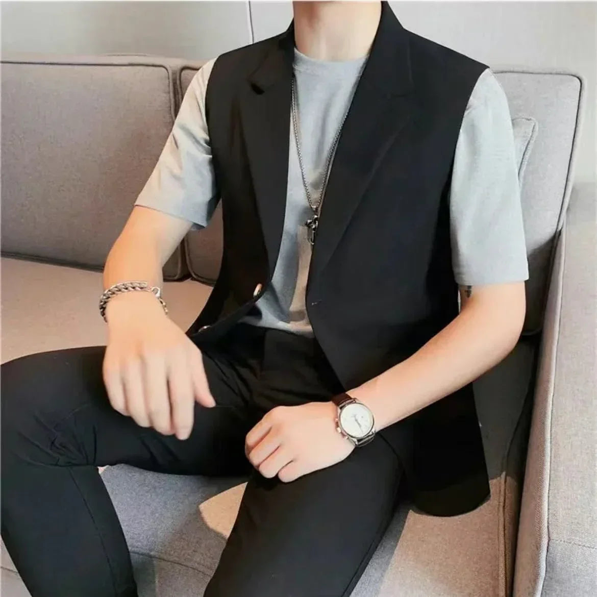 Man wearing a black sleeveless blazer over a light gray t-shirt and black slim fit pants