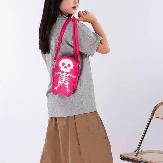 Woman in a loose grey t-shirt and brown skirt, carrying a pink skeleton-print crossbody bag