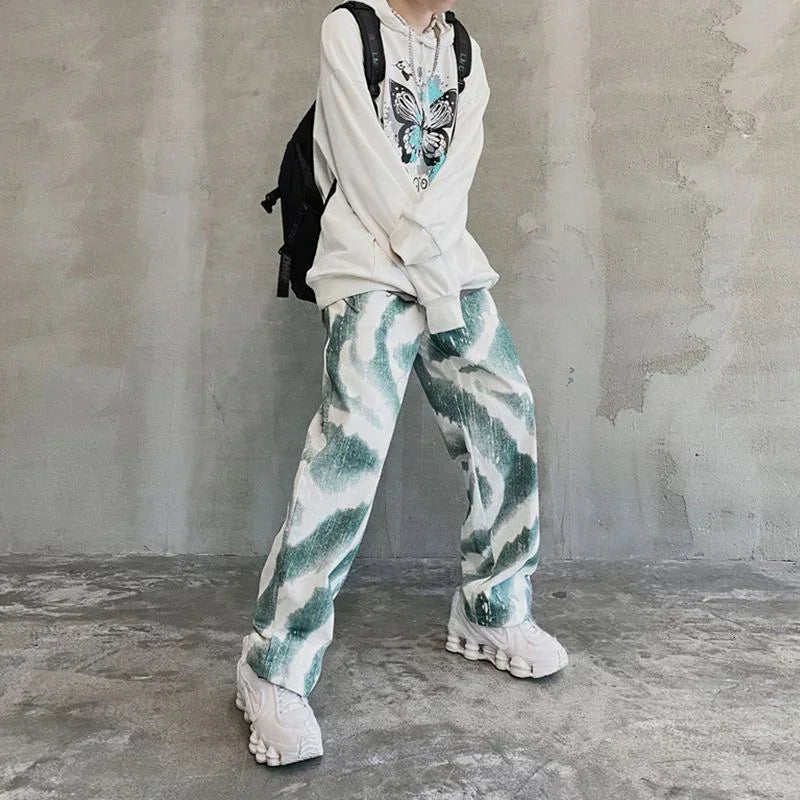 Oversized white hoodie with butterfly print, loose green and white patterned pants, chunky sneakers, streetwear style.
