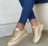 Beige metallic low-top sneakers with gold accents worn with skinny blue jeans