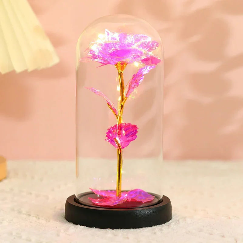 Pink iridescent artificial rose with gold stem in glass dome on black base, decorative lighting