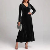 Woman wearing long black velvet A-line dress with V-neck and long sleeves, silver heels