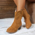 Tan suede mid-calf boots with western stitching, block heel, and relaxed fit on wooden floor