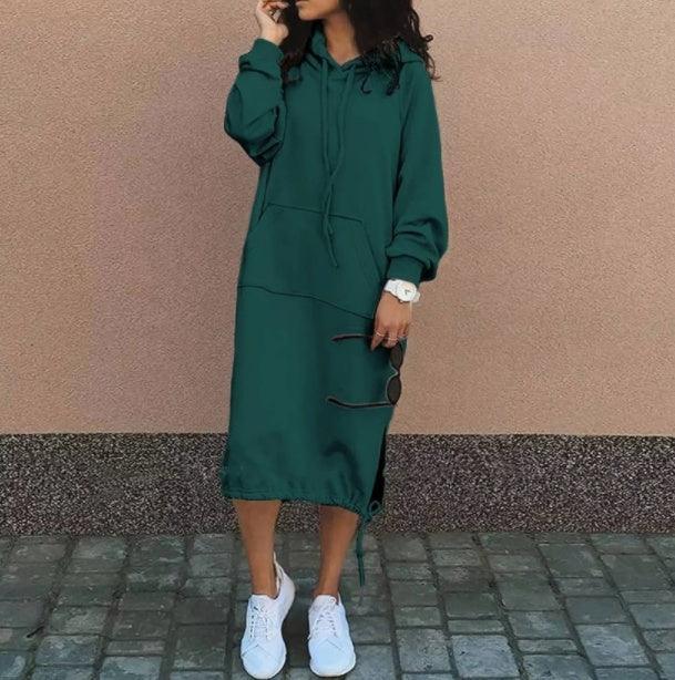 Woman wearing a green oversized hoodie dress with long sleeves and a relaxed fit, paired with white sneakers.