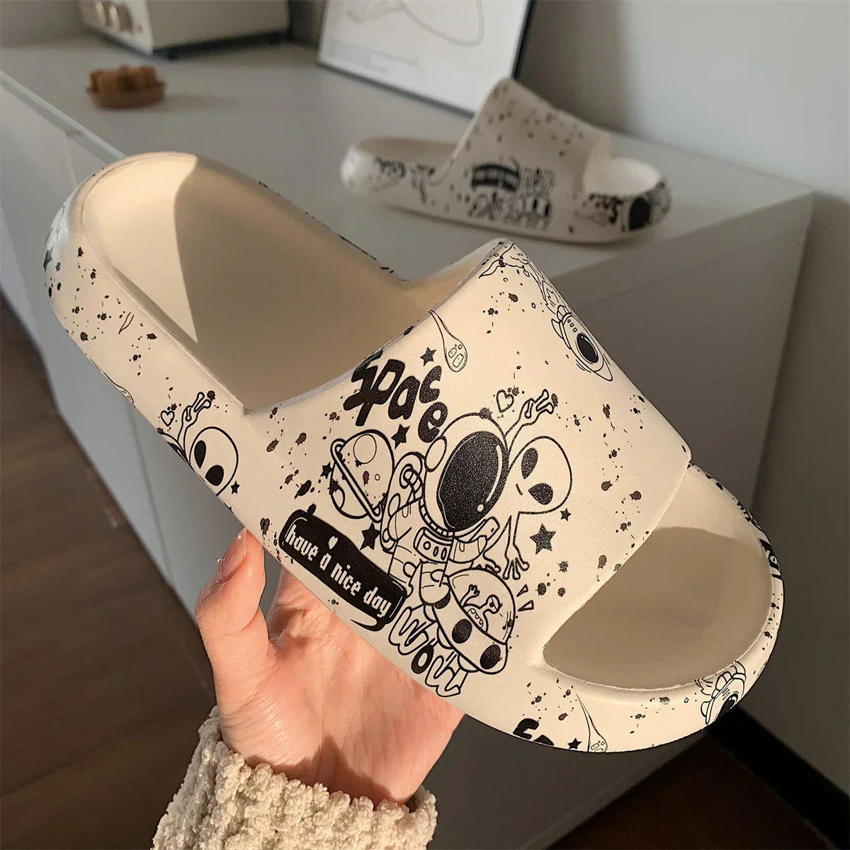 Beige foam slide sandal with black space-themed cartoon print and open toe design