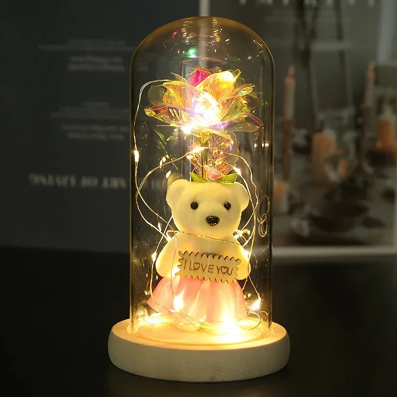 Cute teddy bear in pink tulle dress holding 'I love you' sign under glass dome with LED lights