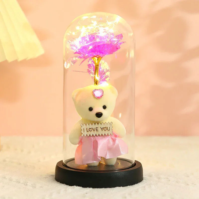 Plush white teddy bear in pink satin dress holding 'I Love You' sign, under glass dome with pink LED rose.