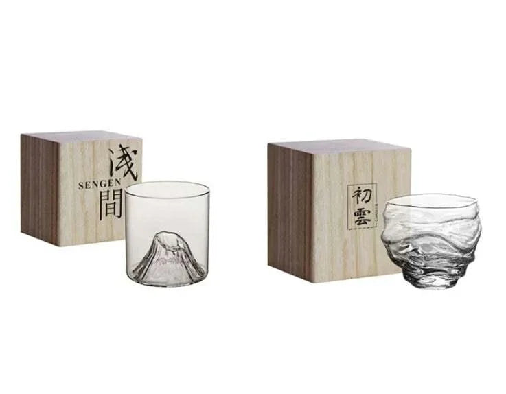 Two clear glass cups with unique mountain and wave designs, displayed beside wooden boxes.