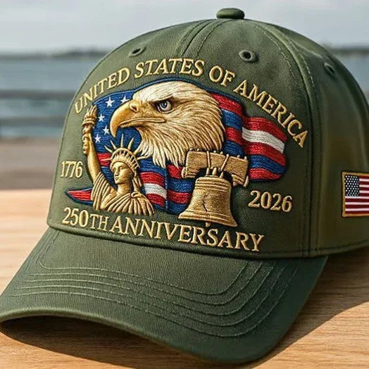 Olive green baseball cap with embroidered bald eagle, Statue of Liberty, Liberty Bell, and American flag, featuring gold anniversary text and an American flag patch on the side.