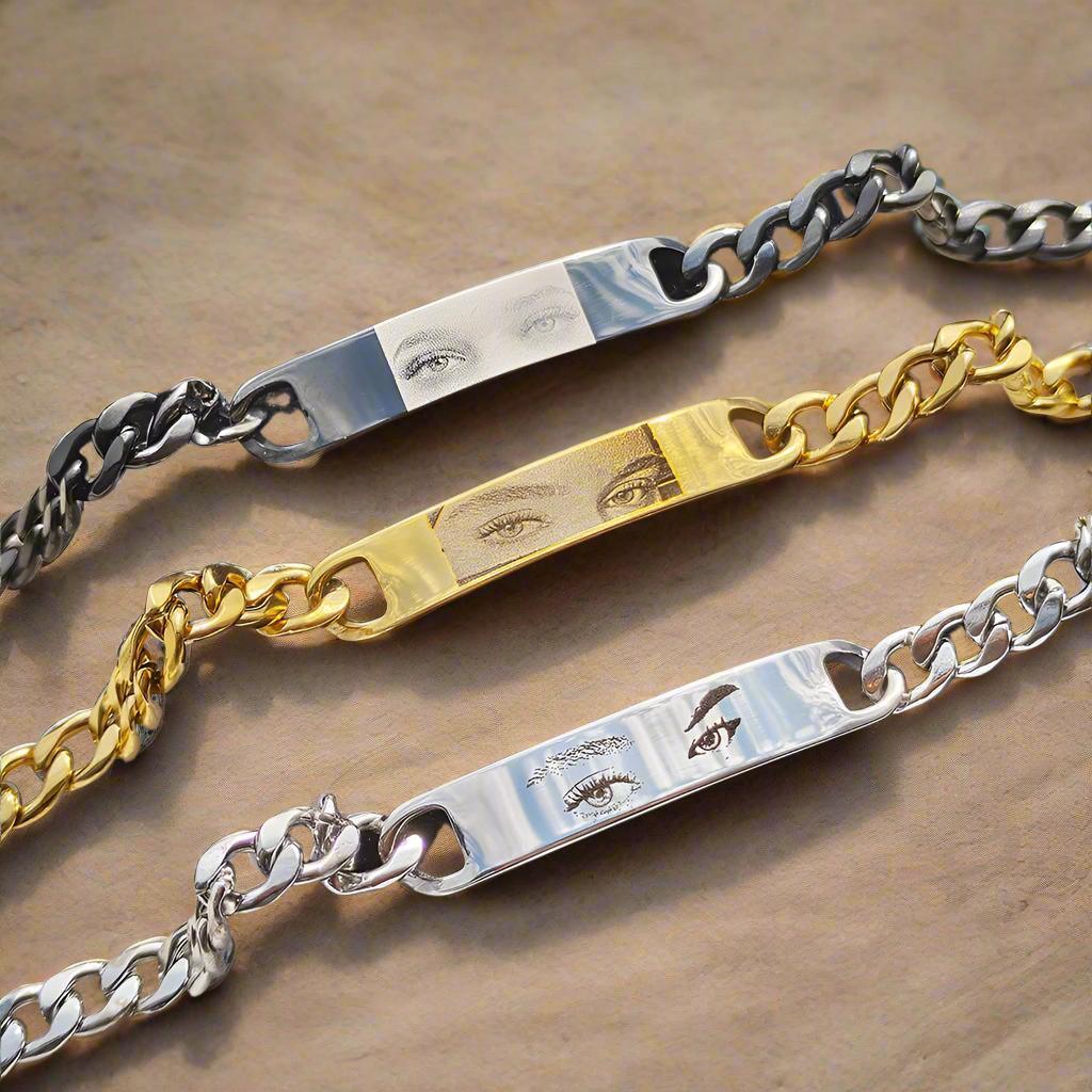 Three engraved chain bracelets in silver and gold tones with eye illustrations on metal plates