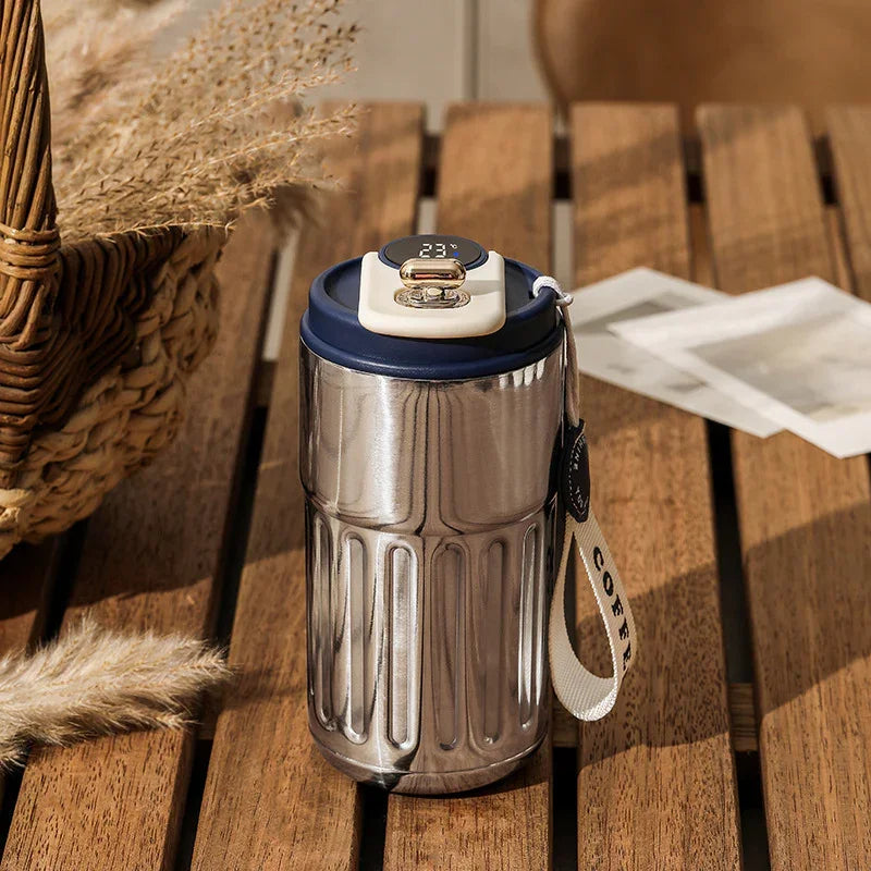Stainless steel insulated tumbler with navy lid, cream handle, and fabric wrist strap on wood table.