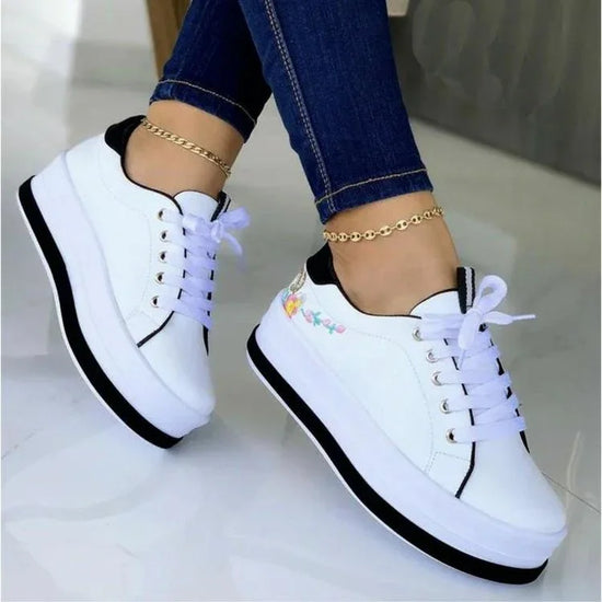 White platform sneakers with black trim, floral embroidery, and chunky sole, styled with skinny jeans.