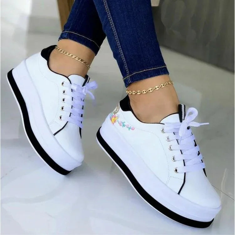 White platform sneakers with black accents and floral embroidery, paired with skinny jeans.
