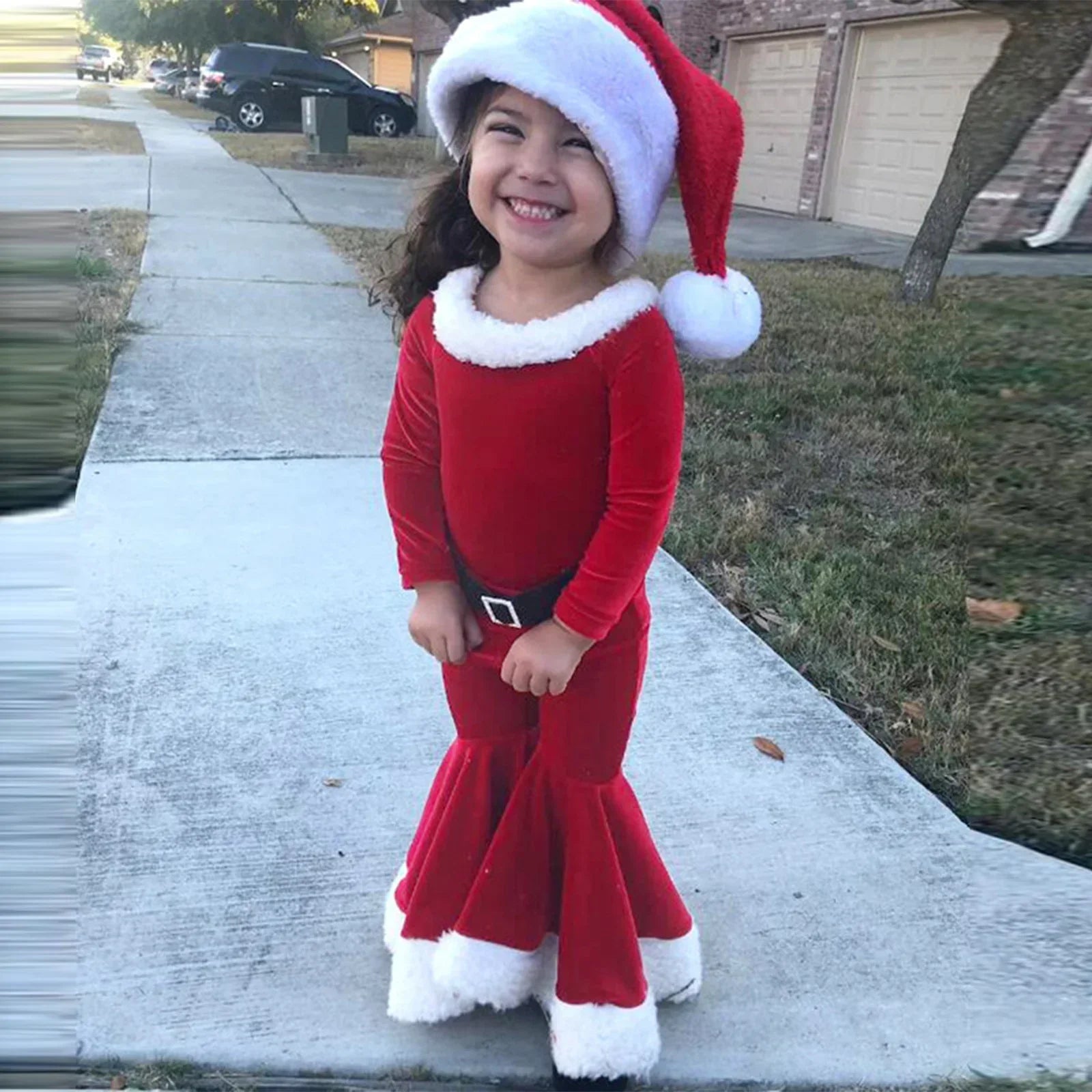 Smiling child in red velvet Santa dress with white faux fur trim and flared skirt outdoors