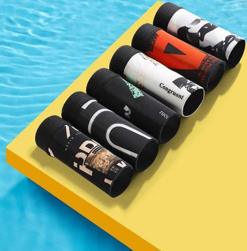 Assorted rolled streetwear graphic t-shirts in bold prints and colors on a yellow surface by a pool