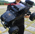 Person holding a large black off-road RC car with rugged tires and metallic details outdoors.