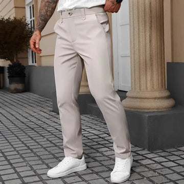 Slim fit beige pants with a smooth finish, styled with white sneakers, outdoor setting.