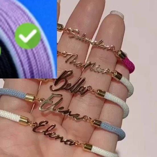 Hand holding personalized name bracelets with gold script lettering and woven colored cords