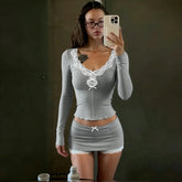 Woman wearing a fitted grey long sleeve top and mini skirt with white lace trim.