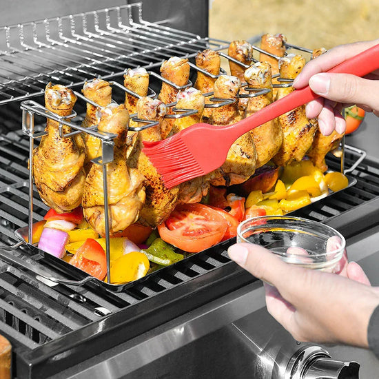 Grilled chicken drumsticks on a rack with vegetables, brushed with marinade on a barbecue.