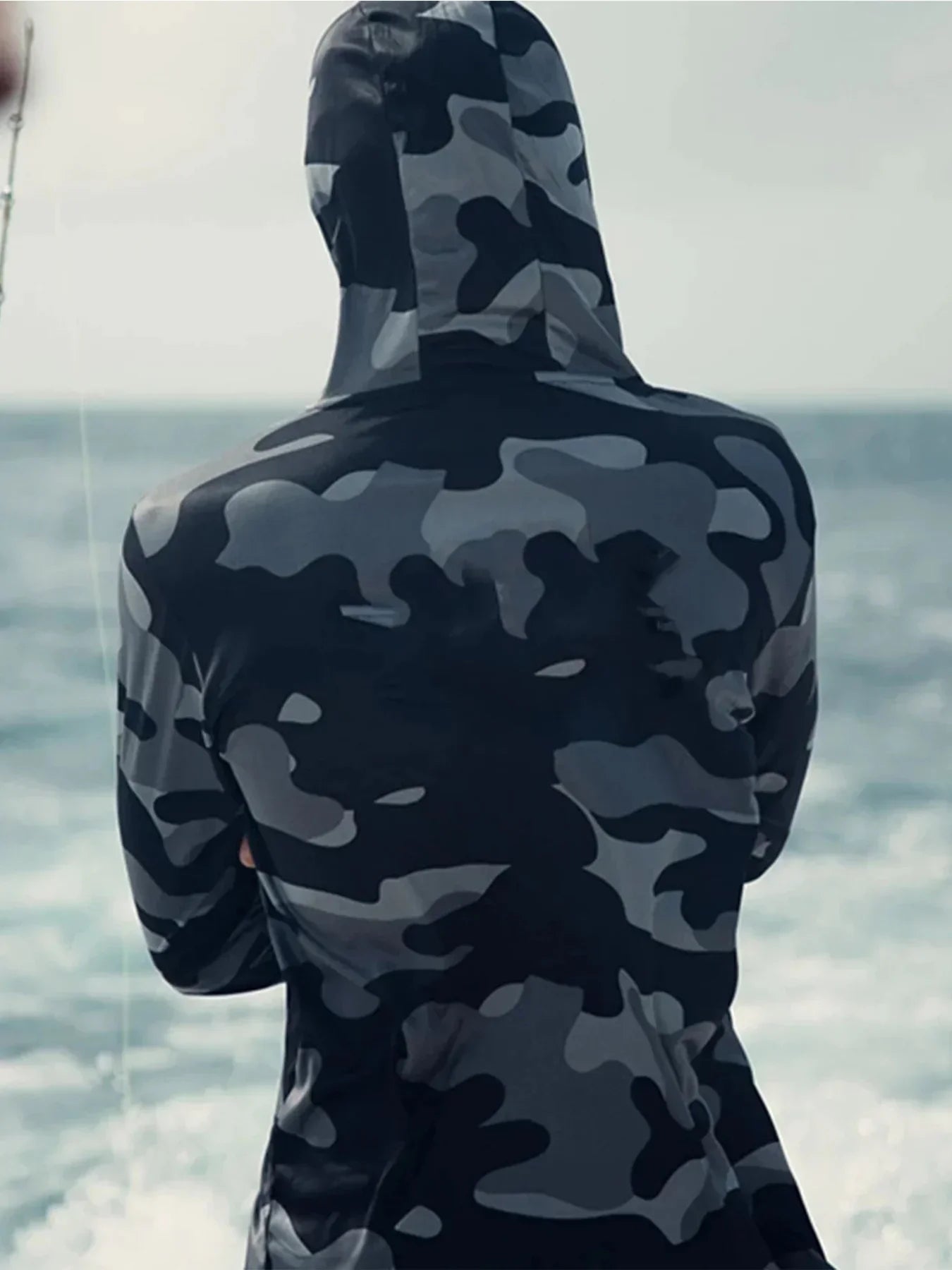 Person wearing a black and grey camo hooded long-sleeve shirt by the ocean