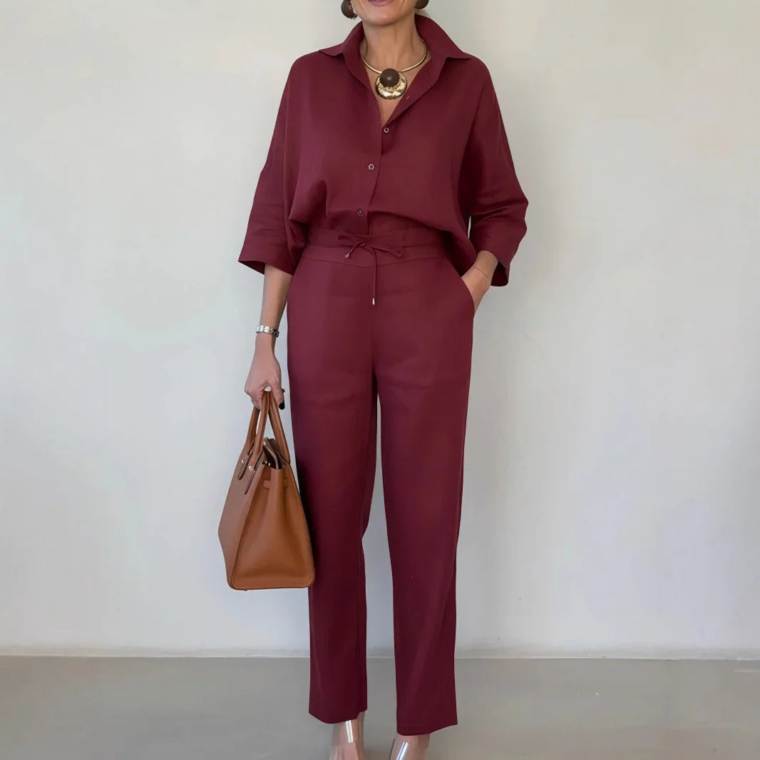 Woman in burgundy relaxed-fit linen shirt and high-waisted pants, holding a tan handbag